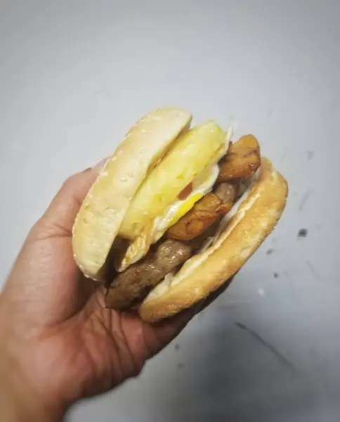 Burger with a juicy beef patty, fried plantains, and a luscious egg between golden sesame seed buns. Unexpectedly delightful: a syrupy pineapple slice for a sweet kick.  Experience the perfect balance of savory and sweet!