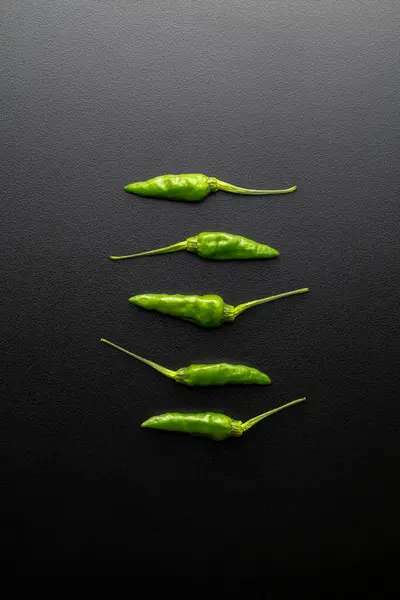 Fresh green chili peppers on black background