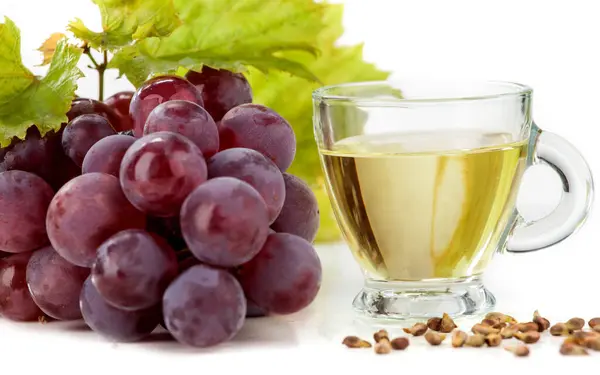 Grape seed oil on white background. The image also shows light grapes and dark grapes arranged on a white background