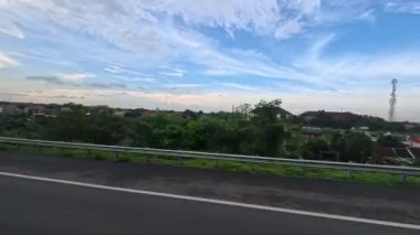 Yolculuğun zamanlaması, mavi gökyüzündeki bulutların arkaplanına karşı yoldan görülen şehri gösteriyor..