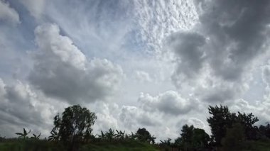 Doğal bir manzarayı gösteren bir yolculuğun yavaş çekimi, yolda görünen ağaçlar, mavi gökyüzündeki bulutların arka planına sahip.