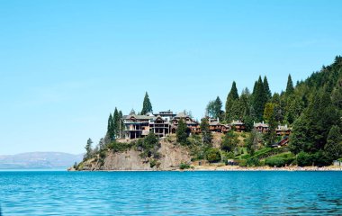 Gölün kıyısındaki binalar ağaçlarla çevrili, gölün ve dağların zeminine karşı..