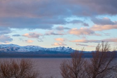Dağların, gölün ve ağaçların üzerinde dramatik bulutlarla akşam gökyüzü. Gölün üzerinde dramatik gün batımı