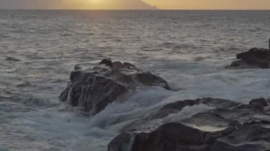 Teno Kanarya Adaları 'ndaki kayalarda dalgaların sıçraması gökyüzünde günbatımının görüntüsüyle.