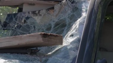 Parçalanmış bir arabanın yakın çekim görüntüsü. Ön cam bir kalasla kırılmış. Araç soyulmuş. Vandalizm. Kamera yavaşça uzaklaşıyor.
