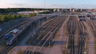 Helsinki. Finlandiya-30 Ağustos 2021: Tren istasyonundan yavaşça geçen bir trenin havadan çekilmiş görüntüleri. İskandinav mimarisi. Arka planda mavi gökyüzü. İnsansız hava aracı yana ve ileri hareket ediyor.