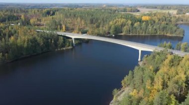 Finlandiya 'daki Saimaa Gölü' nün mavi sularındaki uzun köprü. Bir İHA kamerası renkli orman örtüleri ve göl suyu üzerinde hızla hareket eder. Rus-Fin sınırına yakın. Jeoloji video 44k.