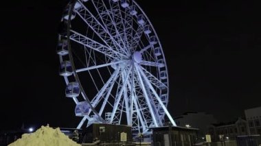 Helsinki. Finlandiya-16 Şubat 2022: Helsinki 'de kışın aydınlatılmış dönme dolap. Yerde kar yığınları var. Aşağıdan yukarıya bak. Kamera sağdan sola hareket eder.