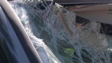 Kırık ön camı gösteren bir arabanın yakın çekim görüntüsü var. Pencere tahta kullanarak kırılmış. Arabaya zorla girilmiş. Kamera yavaşça uzaklaşıyor.