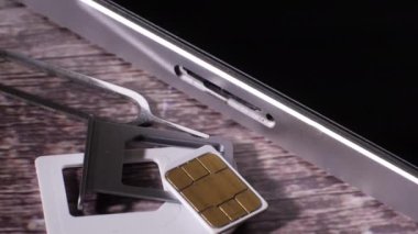 Gümüş renkli akıllı telefonun SIM kart deliğinin yakın plan görüntüsü. Açmak için gerekli aracı göstermek. Modern teknoloji. Ahşap arka. İletişim. Kamera yavaşça hareket ediyor.