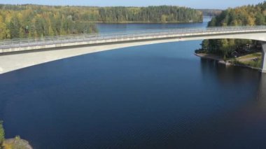 Finlandiya 'da uzun köprüsü olan Saimaa Gölü manzarası. Sonbahar renklerinde orman. Drone kamerası geriye doğru hareket ediyor. Rusya-Finlandiya sınırına yakın. Hava jeolojisi video .4k