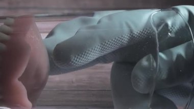 Plastik eldiven kullanılarak bir bardak sudan çıkarılan protez dişlerin yakın çekimi. Yandan ve aşağıdan yukarıya bak. Arka planda tahta tahta var. Dikey Biçim Videosu