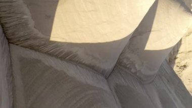 Madencilik alanında açık renkli kum yığınları. Akşam güneşi uzun gölgeler bırakır. İnsansız hava aracı bakış açısı. Kamera yavaşça geriye doğru hareket eder ve yukarı doğru eğilir. Hava jeolojisi fotoğrafı. Dikey Biçim Videosu.