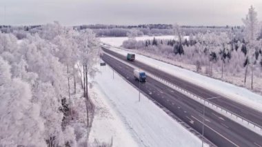 Tallinn.Estonya-4 Şubat 2022: Estonya 'da soğuk bir İskandinav kışında bir otoyolun havadan çekimi. Hava bulutlu. Karlı orman ve toprak. Araba sürüyor. Drone sola dönerken ileri gidiyor. 