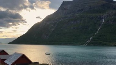 Zaman ayarlı. Norveç 'te fiyort suyunun kenarındaki yerli halkın evlerinin yosun çatısı. Kıyıdan uzakta küçük bir balıkçı teknesi. Hızlı su hareketi. yakınlaştır