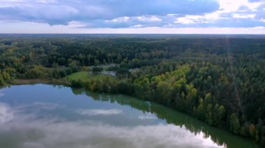 Finlandiya 'daki karavan bölgesinde gölün kenarındaki ağaçlar gökyüzündeki bulutların yansıması. Kamera yavaşça geri ve yukarı hareket eder.