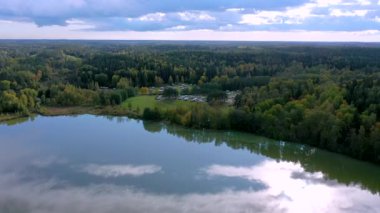Finlandiya 'daki karavan bölgesinde, ağaçların kenarındaki gölün mavi suları. Kamera yavaşça geri gidiyor..