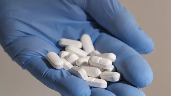 Elinde beyaz haplar tutan lastik eldivenli bir elin yakın çekimi. İnsanlara ilaç konseptini vermek. İlaç endüstrisi.. 
