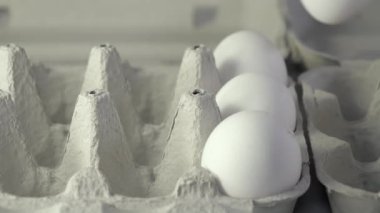 Yumurtaları bir eliyle bir yumurtalıktan diğerine taşıyor. Bir sürü büyük beyaz yumurta var. Arka plan bulanık. Yakın çekim..