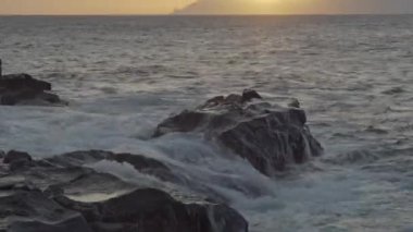 Kanarya Adaları 'ndaki kayalıklarda gün batımını gören dalgalar. Ufukta bulutlar var. Jeoloji fotoğrafı. Kamera yavaşça yukarı doğru yükseliyor. 