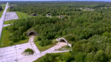 Estonya, Haapsalu-21 Temmuz 2019: Terk edilmiş askeri üs havaalanının uzun pisti ile birlikte hangarın kenarındaki orman ağaçlarının havadan çekilmiş görüntüleri. Kamera yavaşça geriye hareket ediyor..