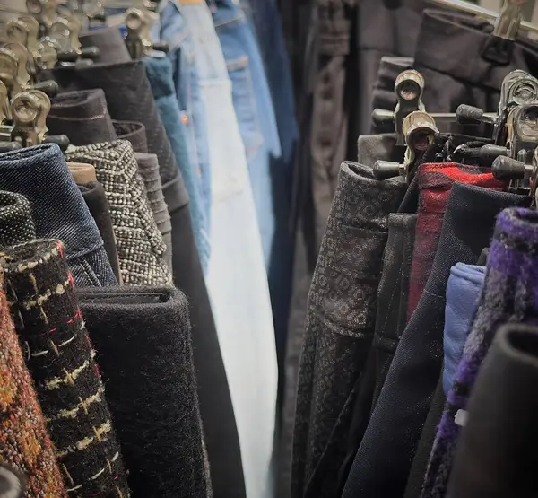 Alışverişçiler, askılarda özenle düzenlenmiş, sürdürülebilir moda uygulamalarını desteklemek amacıyla çeşitli dokular ve renkler sergileyen geri dönüşümlü giysilerin bir koleksiyonunu keşfediyorlar..