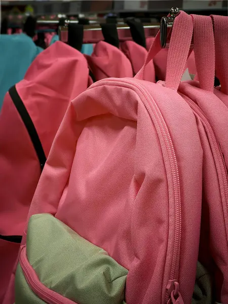 İki pembe sırt çantası bir perakende mağazasında bir askıda duruyor, renkli ve değişik dokular sergiliyorlar, müşterileri gün boyunca şık tasarımlarını keşfetmeye çağırıyorlar..