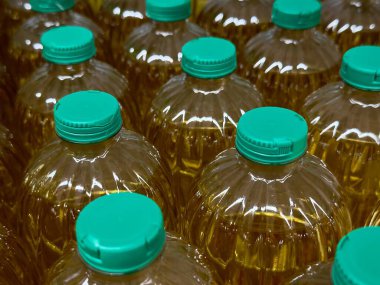 İçi yemek yağı dolu şeffaf şişelerin sergilendiği, bir market koridorunda düzenlenen turkuaz şapkaların sergilendiği bir sergi. Yağların canlı rengi deponun arka planıyla çelişiyor.