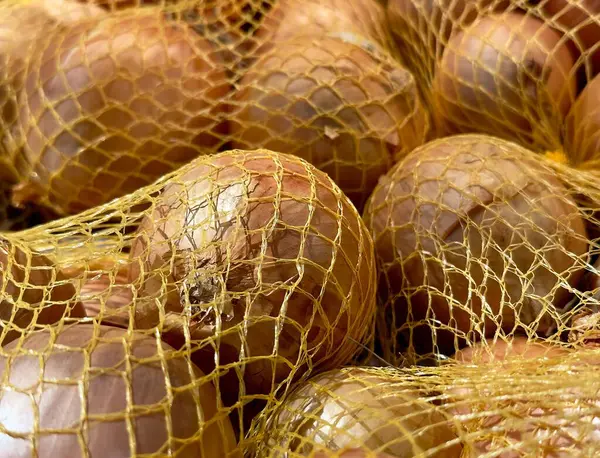 Manzara, markette düzgünce yerleştirilmiş ağlı poşetlere doldurulmuş taze soğanları gösteriyor. Müşteriler bu sebzeleri yemek ihtiyaçları için kolayca seçebilirler..