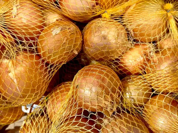 Çeşitli taze soğanlar ağlı poşetlerde düzgünce paketlenerek toprak tonlarını sergiliyorlar. Bu soğanlar marketlerde belirgin bir şekilde sergileniyor. Üretim bölümünde, tazelik vurgulanıyor..