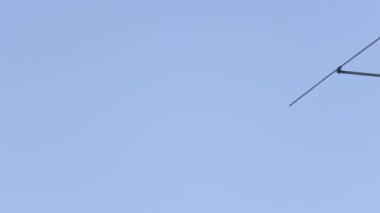 Arka planda açık gökyüzü olan bir direğe bağlı antenlerin yakın çekim görüntüleri. Televizyon için kullanılan antenler. Kamera yavaşça sağa hareket ediyor.