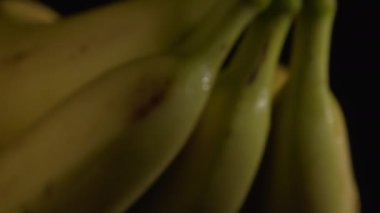 Kameranın önünde dönen nemli muzların yakın plan çekimi. İştah açıcı ve iyi bir vitamin kaynağı olarak kullanılan taze sebzeler. Sağlıklı beslenme alışkanlıkları. Siyah arka plan. Dikkati dağılmış. Seçici odak.