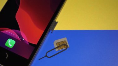 Akıllı telefon ve arkasında Ukrayna bayrağı olan sim kart. Savaş sırasında iletişim. Bazı şirketler Ukrayna 'ya ücretsiz telefon sağlıyor. Kamera yavaşça yana hareket ediyor. - Yakın çekim. Metin uzayı.