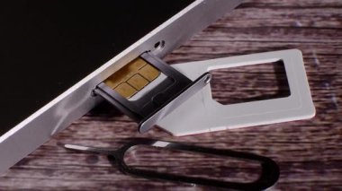 Yakın çekim, gümüş renkli akıllı telefonun sim kart yuvasını gösteriyor. Alet açmak için gerekliydi. İletişim. Modern teknoloji. Ahşap arka. Kamera yavaşça hareket ediyor.