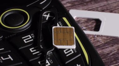 Siyah ve sarı bir cep telefonunun ve sim kart yuvasının parçalarının yakın çekimi. Ahşap arka. İletişim. Açmak için gerekli aracı göstermek. Kamera yavaşça uzaklaşıyor.