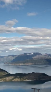 Norveç 'teki fiyordun güçlü doğal manzarası. Mavi gökyüzünde beyaz bulutlar var. Zaman ayarlı. Kamera sola hareket ediyor. Dikey video