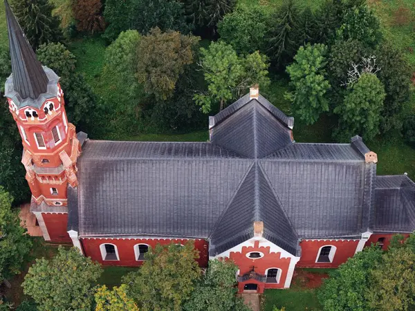 Halliste, Estonia September 25, 2025: Red brick church with tall steeple and dark gray roof, nestled among green trees, photographed from a high aerial viewpoint
