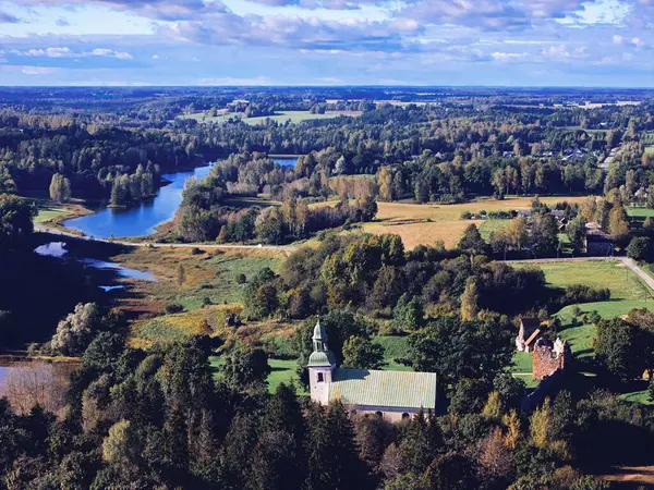 Karksi, Estonya 25 Eylül 2025: Tarihi Karksi Lutheran Kilisesi, kale kalıntıları ve orman ve tarlalarla çevrili dolambaçlı bir nehir ile Güney Estonya manzarası