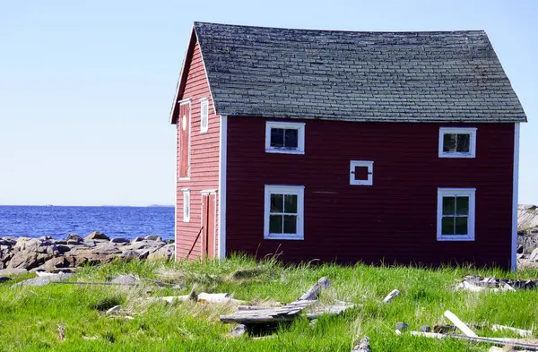 Newfoundland 'daki Fogo Adası kıyısındaki çimenli bir arazide kırmızı ahşap bir ev.