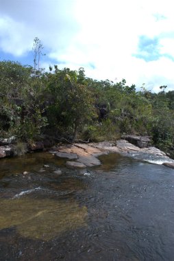 Arkasında kayalar ve ağaçlar olan bir nehir.