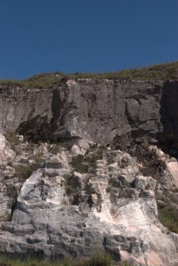 Sörf tahtasıyla kayanın üzerinde duran bir adam.