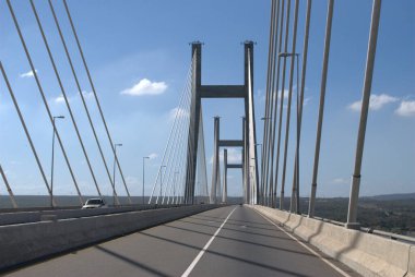 Gökyüzü arkaplanı olan bir köprüde giden bir araba.