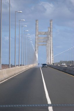 Gökyüzü arkaplanı olan bir köprüde giden bir araba.