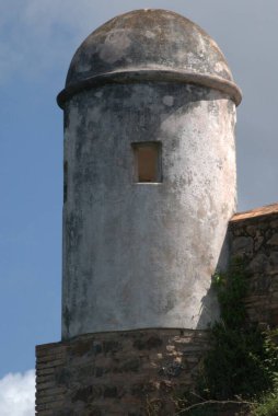Mavi gökyüzünün altındaki yuvarlak bir taş binanın dikey görüntüsü.