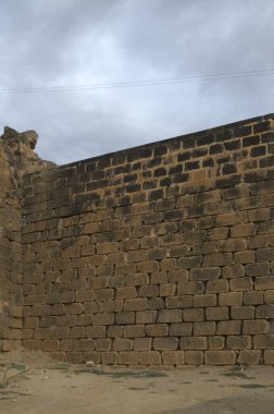 Tuğla duvarın dikey bir görüntüsü ve tarlanın ortasında büyük bir taş duvar var.