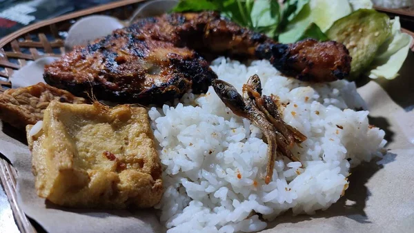 Lalapan adlı geleneksel Endonezya yemeği ahşap tabakta ızgara tavuk ve ızgara balık, sebze, kızarmış tempeh ve baharatlı acı biber soslu pilav var.