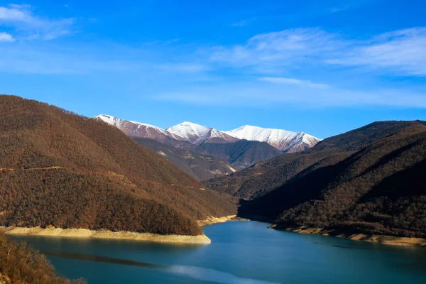 Gürcistan dağları sonbaharın sonunda. Mavi göl ve karlı tepelerin manzarası çok güzel. Yolculukta güneşli bir gün