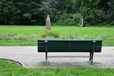 Huzurlu açık hava manzarası bankın önünde kaldırımlı bir yol gösteriyor. Yaz boyunca halka açık bir parkta dinlenmek ve doğanın tadını çıkarmak için mükemmel.