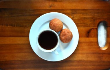 Tahta masadaki beyaz tabakta servis edilen iki taze çörekle bir fincan sade kahve. Minimalist kahvaltı konsepti, üst manzara.