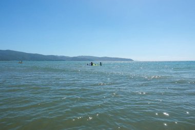 Bir grup insan bir su kütlesinin içinde. Güzel deniz manzarası. Panorama. Mavi deniz ve mavi gökyüzü arka planı. Yaz denizi ve mavi gökyüzü. Kumsaldaki dalgalarla birlikte denizin panoramik görüntüsü. Kumsalda deniz dalgaları